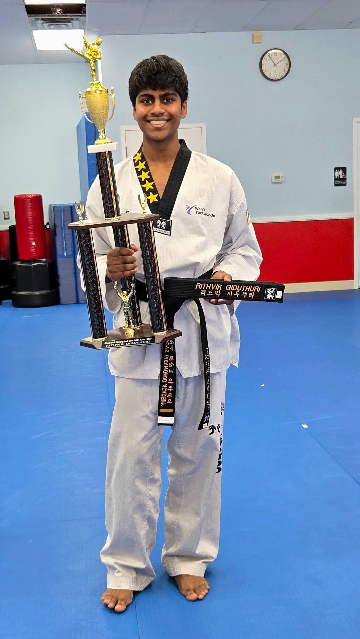 Rithvik holding his black belt and taekwondo trophy